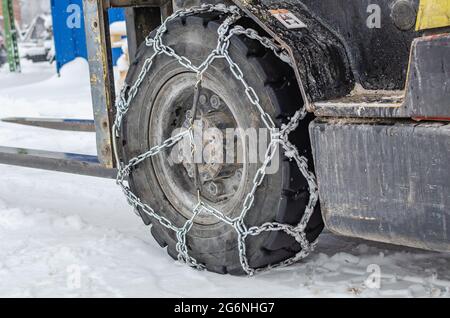 The loader is driving in the snow, the wheels are equipped with chains. Winter snowy day Stock Photo