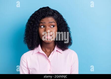 Photo of pretty doubtful dark skin woman wear pink outfit biting lip looking empty space isolated blue color background Stock Photo