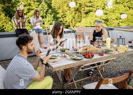 People spending time together, sitting separately in smart phones at party outdoors Stock Photo