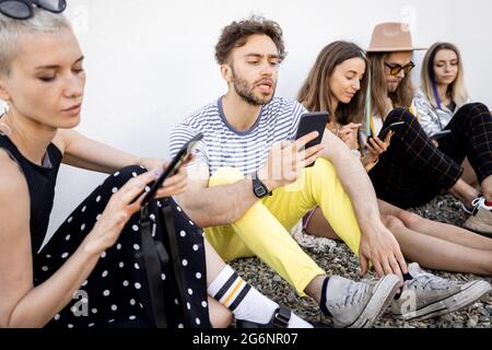 Friends sitting in a row with smartphones Stock Photo
