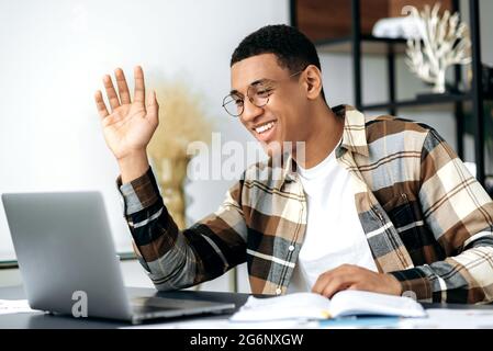 Online video communication. Positive successful latino guy, freelancer, designer or student, sits at his desk, using a laptop for communication via video call, talking to a colleague or friend, smiles Stock Photo