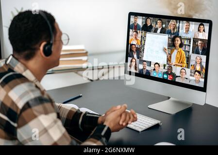 Online education, webinar, lecture. Male student studying online, on computer screen are multiracial people, female teacher conducts online lesson for students by video call, virtual learning concept Stock Photo