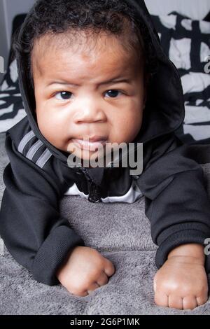 Charismatic 4 months old baby boy. A little toddler. Hip hop baby boy. Portrait of a cute urban baby, wearing a grey adidas outfit. Stock Photo