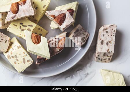 Pieces of different types of halva on a gray plate, white marble background. Middle eastern dessert concept. Healthly food. Stock Photo