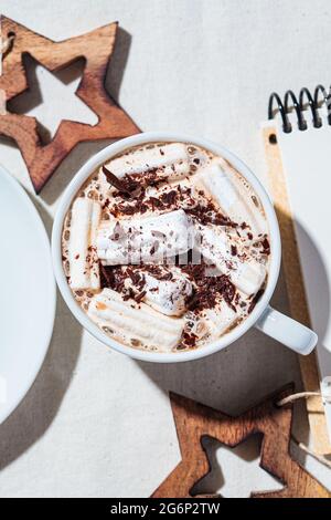Christmas or New Year festive background. Hot chocolate or cocoa with marshmallows in a cup, christmas decorations, top view, white fabric background. Stock Photo