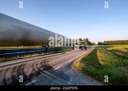 Heavy transport: Wind turbine propeller blade transportation on small countryside road, escorted by security car. Sunny Summer evening. Close up photo Stock Photo