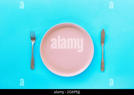 Empty pink plate with fork and knife on blue background. Diet concept. Top view, flat lay Stock Photo