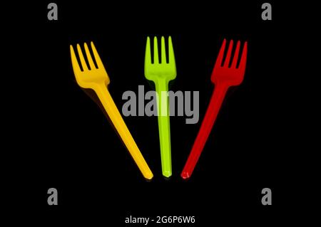 Three plastic disposable utensil cutlery forks yellow, green and red (Lithuania flag colors) isolated on the black background Stock Photo
