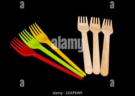 Plastic disposable utensil cutlery forks versus biodegradable wooden disposable utensils isolated on the black background Stock Photo