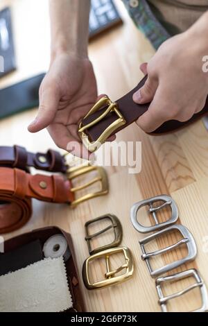 Closeup hands of professional tanner choosing belt buckle on wooden table at leather workshop Stock Photo