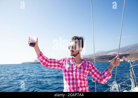 A man in the boat is happy and raises a glass with a drink. it is summer and the sky is clear. Carefree boy, freedom and happiness concept Stock Photo