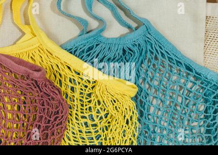 Blue, yellow, pink, beige reusable cotton mesh bags on beige background. Eco-friendly shopping bag. Close up. Zero waste grocery concept. Stock Photo