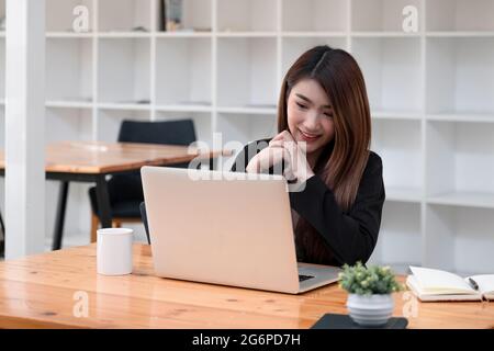 Charming woman looking and speaking through the webcam while making a video conference with laptop from the office. business using laptop computer Stock Photo