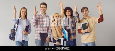 Group of active students in casual clothes raise their hands while standing on a gray background. Stock Photo