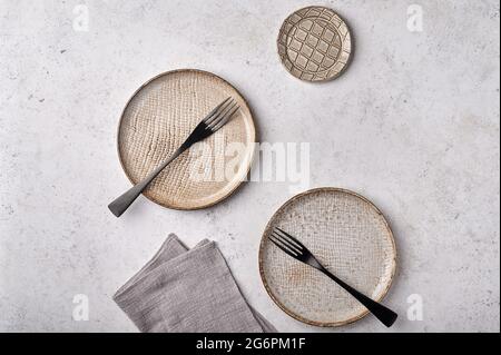 Empty light textured plates with forks and napkin set on gray background. Top view, copy space Stock Photo