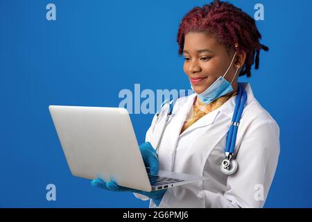 Young african american woman doctor using laptop against blue background Stock Photo