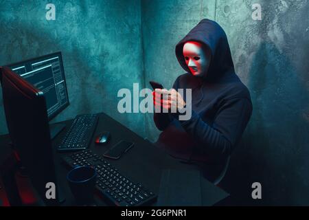 Anonymous hacker wearing face mask working on computer in dark room Stock Photo