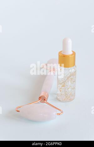 Massage roller for the face made of rose quartz with bottle of 24k gold serum on a blue background. The concept of skin care at home Stock Photo