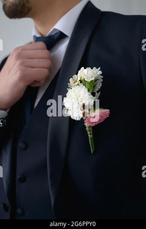 Groom in a dark blue suit with a boutonniere adjusts his tie looking to the side in close-up Stock Photo