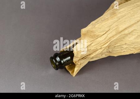 Bottle in paper bag lying on gray background. Dark empty bottle of alcohol in a crumpled brown bag. Close-up. Selective focus. Stock Photo