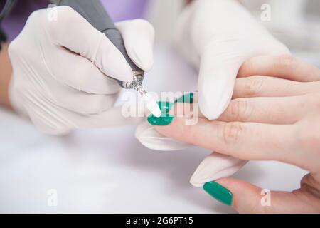 Woman having green nail gel removed by professional manicurist using nail drill Stock Photo