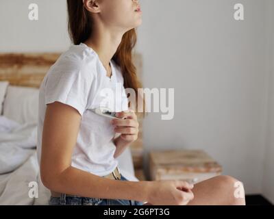 woman sitting on bed with thermometer armpit checking temperature Stock Photo