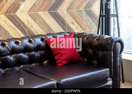 Big comfortable black leather sofa with red pillow in the furniture store. Stock Photo