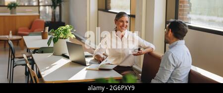 Female discussing new project with male colleague. Mature woman talking with young man in office. Stock Photo