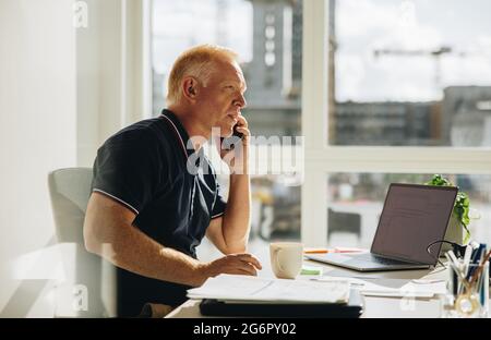 Senior businessman talking on phone. Office manager making a phone call while sitting at his desk. Stock Photo