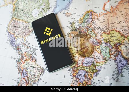 SWANSEA, UK - JULY 8, 2021: Binance app logo on a smartphone and crypto coins Bitcoin, Ethereum and XRP on a world map. Popular cryptocurrency exchang Stock Photo