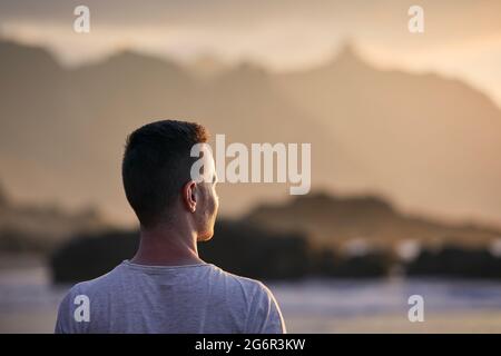 Portrait of pensive man on beach aganinst cliff at golden sunset. Tenerife, Canary Islands, Spain. Stock Photo