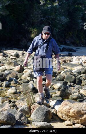 An older man is jumping across rocks on the shoreline Stock Photo