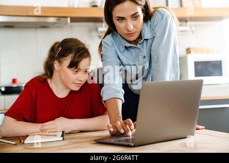 White woman helping her daughter with down syndrome using laptop at home Stock Photo