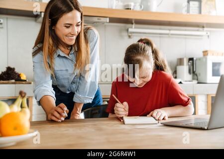 White woman helping her daughter with down syndrome doing homework at home Stock Photo