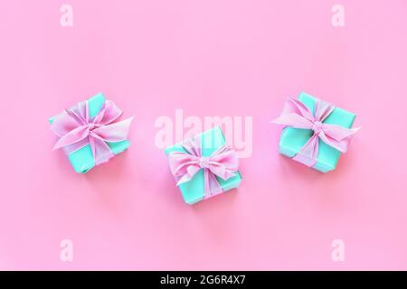 Three green present boxes with bow on pink background. Top view, flat lay. Stock Photo