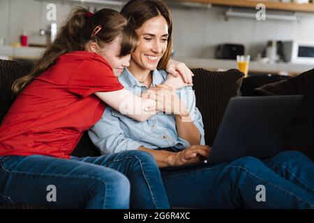Woman and her daughter with down syndrome using laptop while sitting on sofa at home Stock Photo