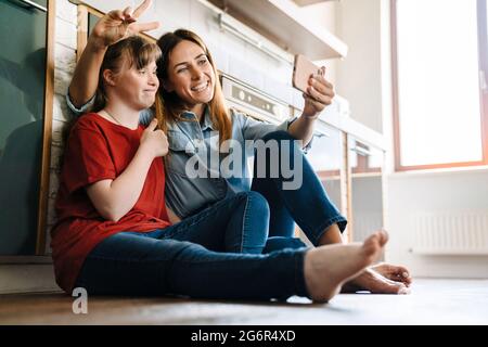 Woman and her daughter with down syndrome using cellphone while sitting on floor at home Stock Photo