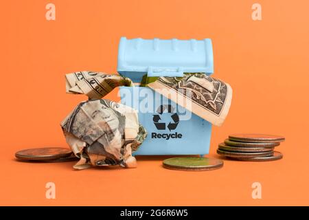 Saving with recycling shown by a light blue recycle bin full of dollar bills on orange background Stock Photo