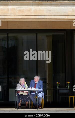A senior couple have lunch outside the café at Weston library, university of Oxford, England, on a sunny summer day. Stock Photo