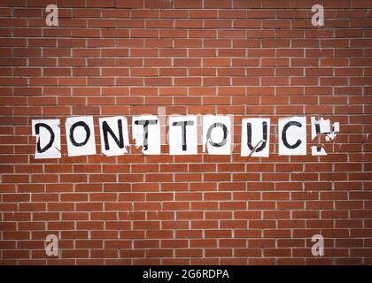 Do not Dont touch message on red brick building wall concept. Message sign ripped and torn stuck onto textured background. Stock Photo