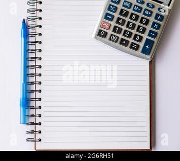 Blank Opened Spiral Notebook With Calculator And Pen Placed Over Table. Empty Lined Notepad And Pencil On Top Of Desk With Calculation Device. Stock Photo