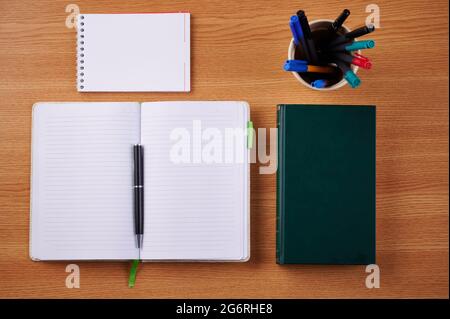 Plain Blank Open Notebooks With Stack Of Pens Inside Container Placed On Top Of A Table. Simple Empty Lined Notepads Beside A Holder Of Colorful Stock Photo