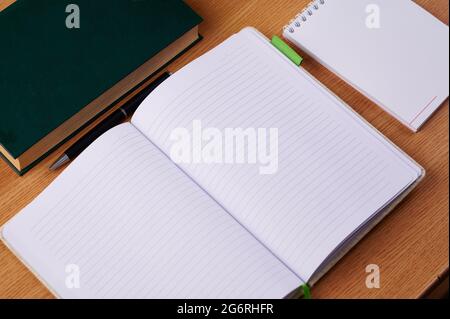 Plain Blank Open Notebooks With Stack Of Pens Inside Container Placed On Top Of A Table. Simple Empty Lined Notepads Beside A Holder Of Colorful Stock Photo