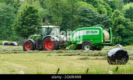 Hay & silage making (farmer in farm tractor at work in rural field, collecting cut dry grass, unwrapped round bale in baler) - Yorkshire England, UK. Stock Photo