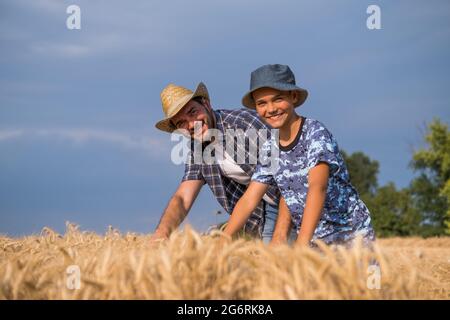 Happy father and son are standing in their grown wheat field before harvest. Stock Photo
