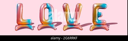 some multicolored letter-shaped balloons forming the word love on a pink background,  in a panoramic format to use as web banner or header Stock Photo