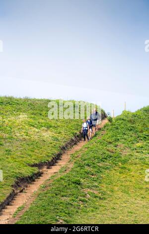 Walkers walking down a set of steps on a steep sloping footpath near Mawgan Porth in Cornwall UK. Stock Photo