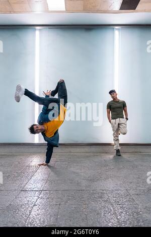 Two multi-ethnic friends dancing break dance and having fun against white wall with lights. Stock Photo