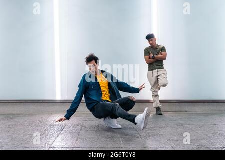 Amazing young men practicing break dance together against white wall with lights. Stock Photo
