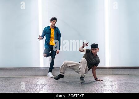 Two multi-ethnic friends dancing break dance and having fun against white wall with lights. Stock Photo
